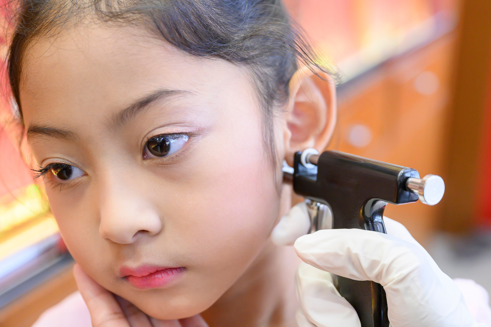 Adorable little asian girl having ear piercing process.