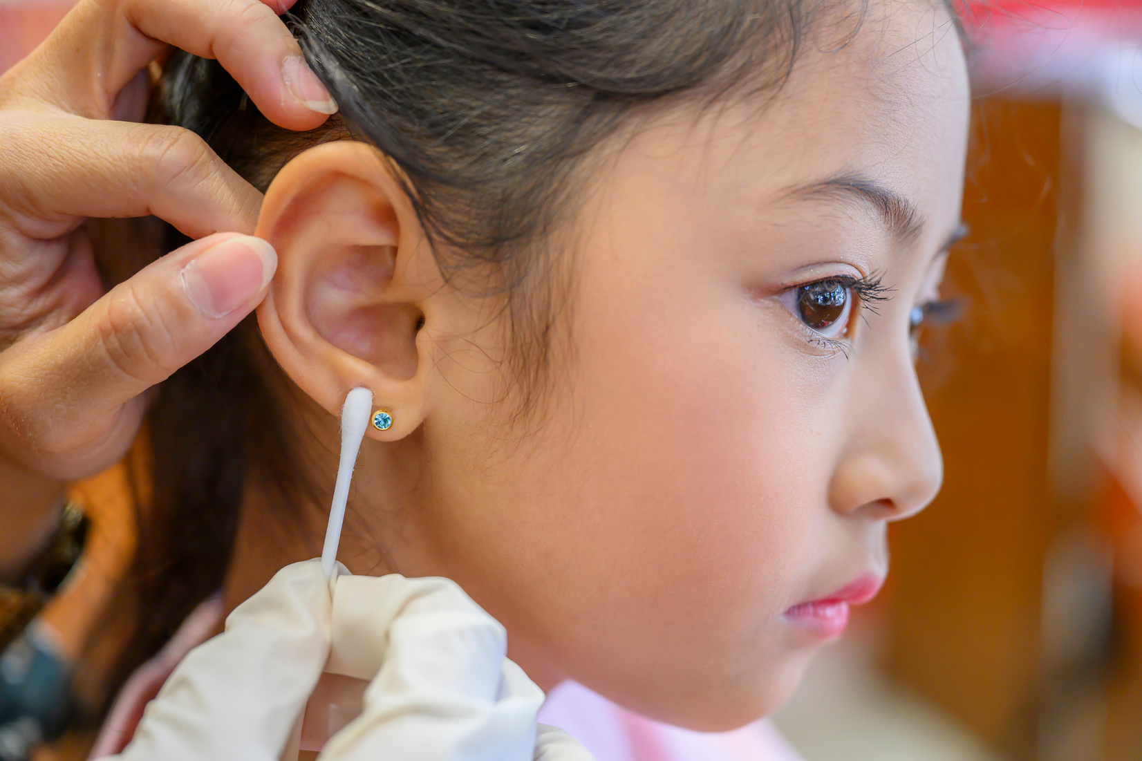 Adorable little asian girl having ear piercing process.